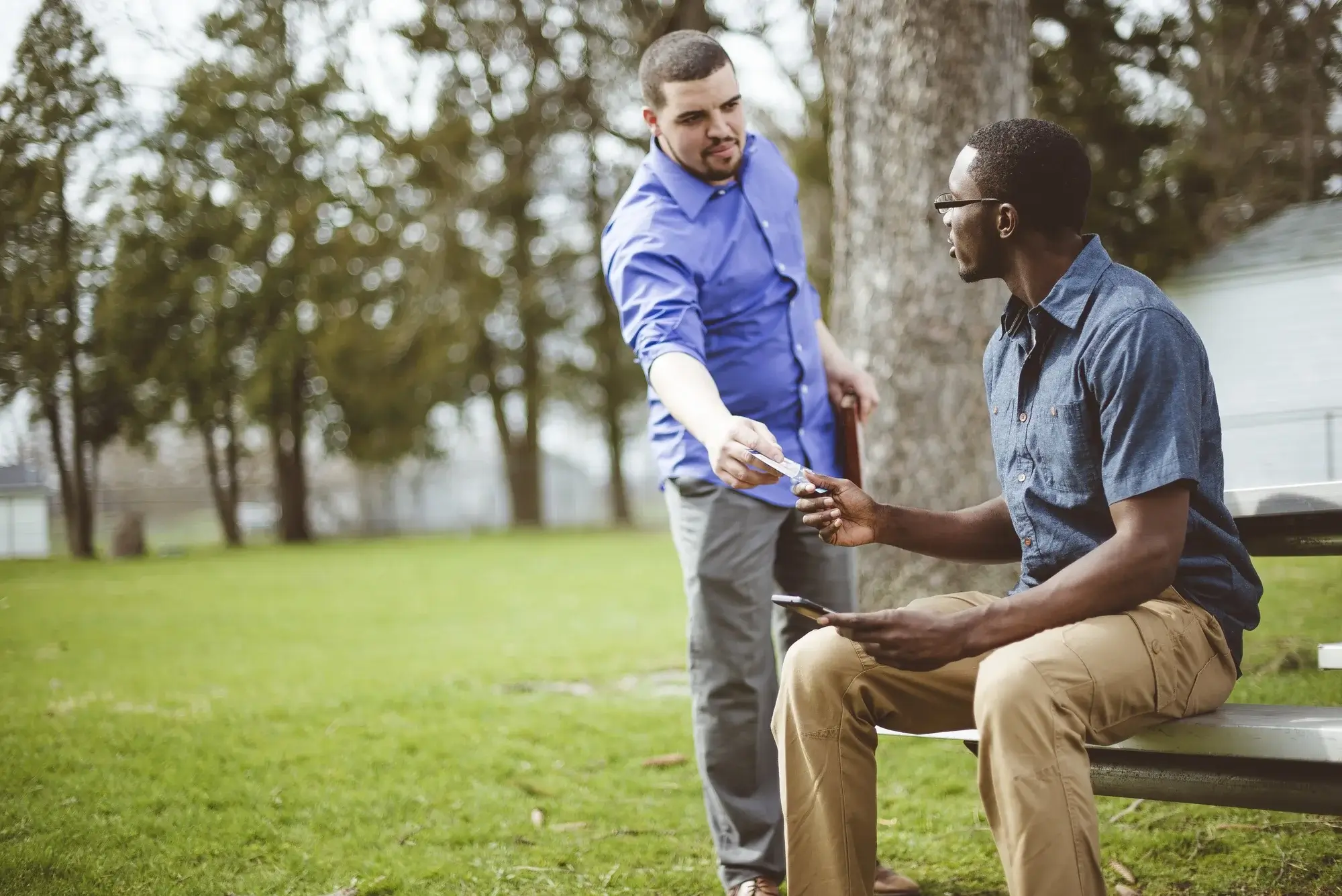 A man hands a card to another man on a bench, illustrating the simple insurance verification step of the rehab admissions process.