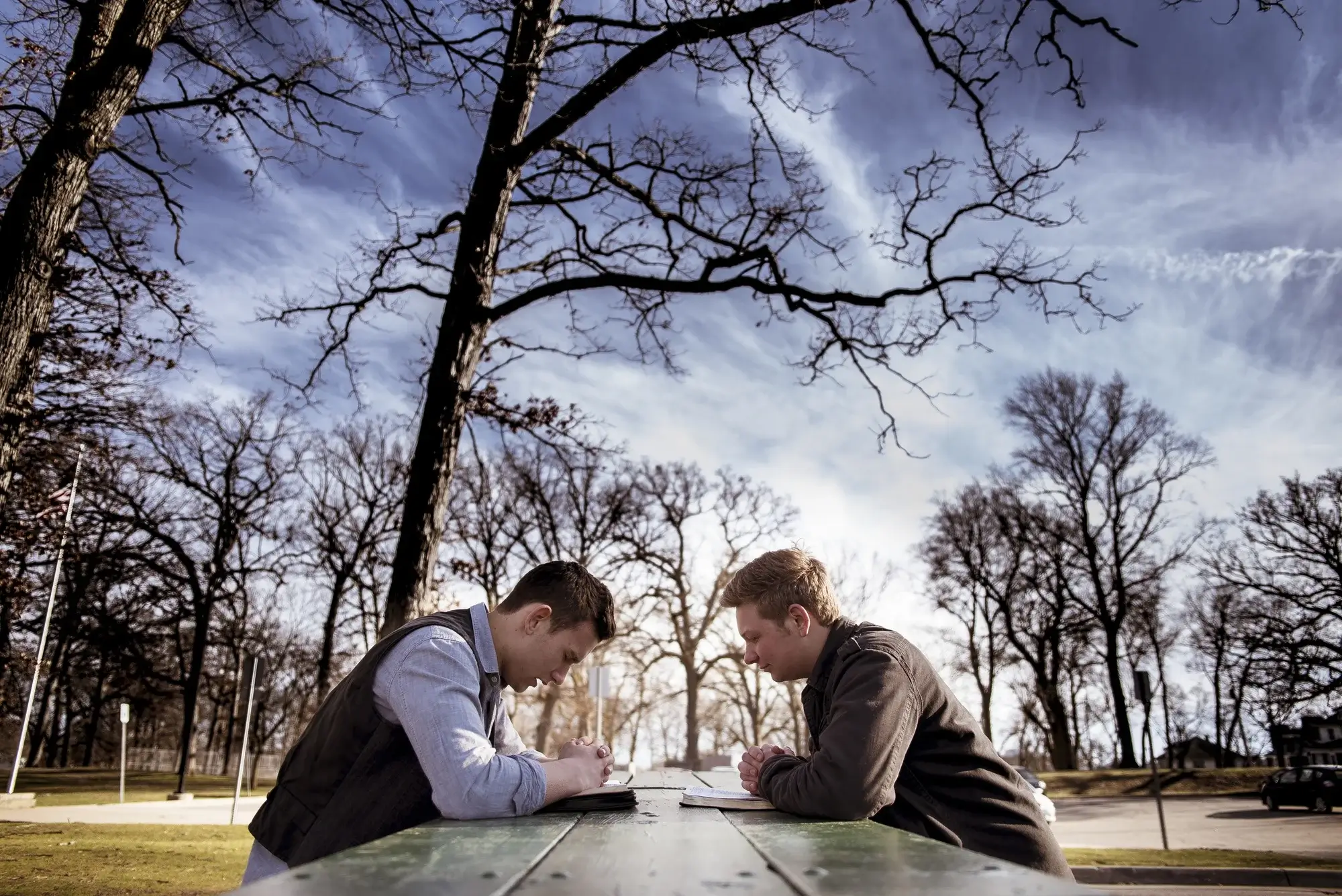 Two men sit in solemn contemplation outdoors, highlighting the serious risks addressed by heroin addiction treatment in Missouri.