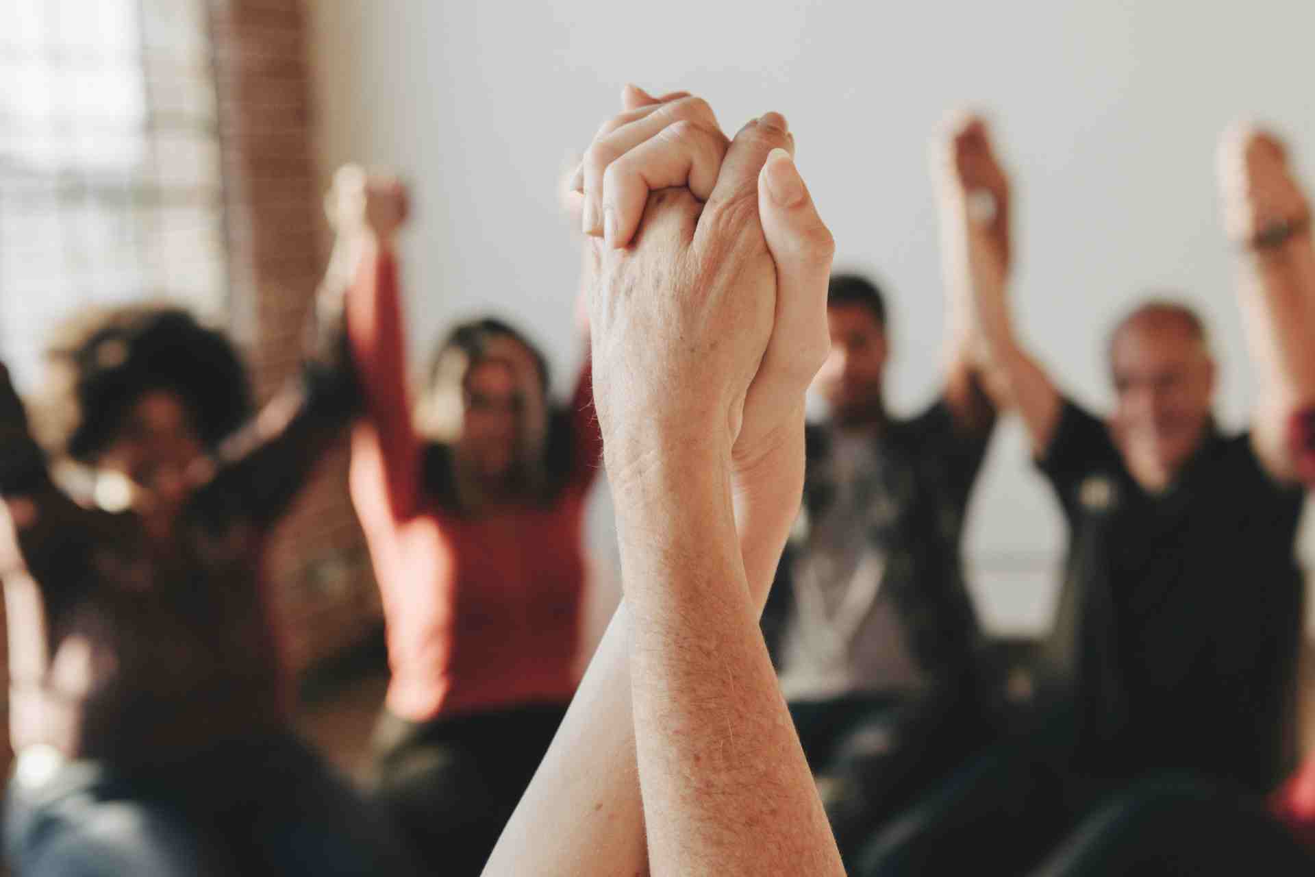 People in addiction recovery support group holding hands in unity
