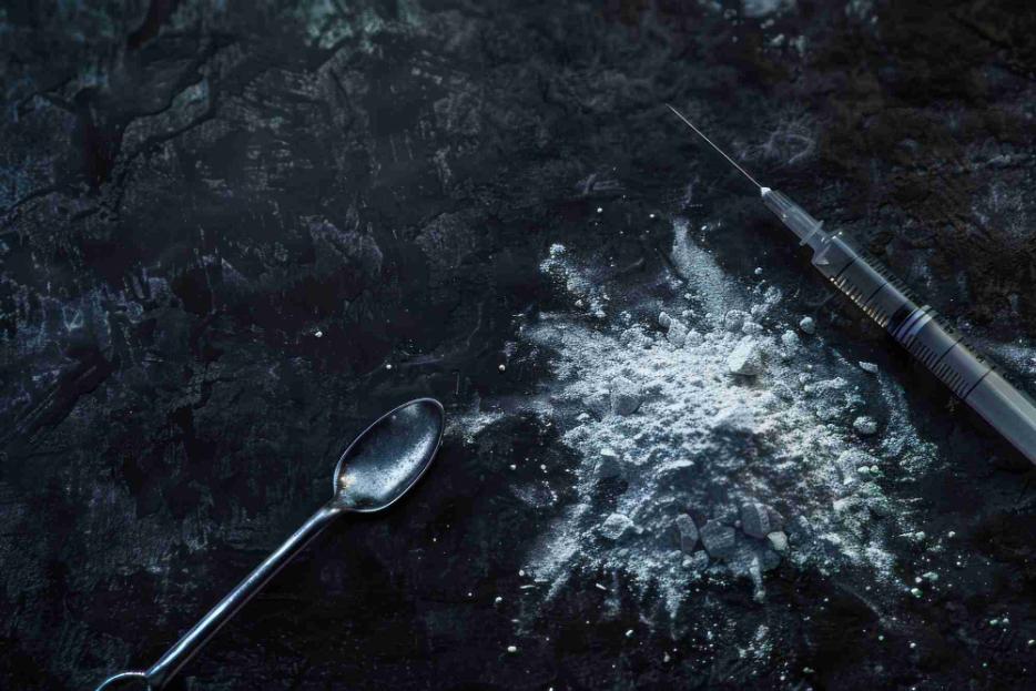Syringe and heroin powder on dark surface representing injection drug abuse and opioid addiction