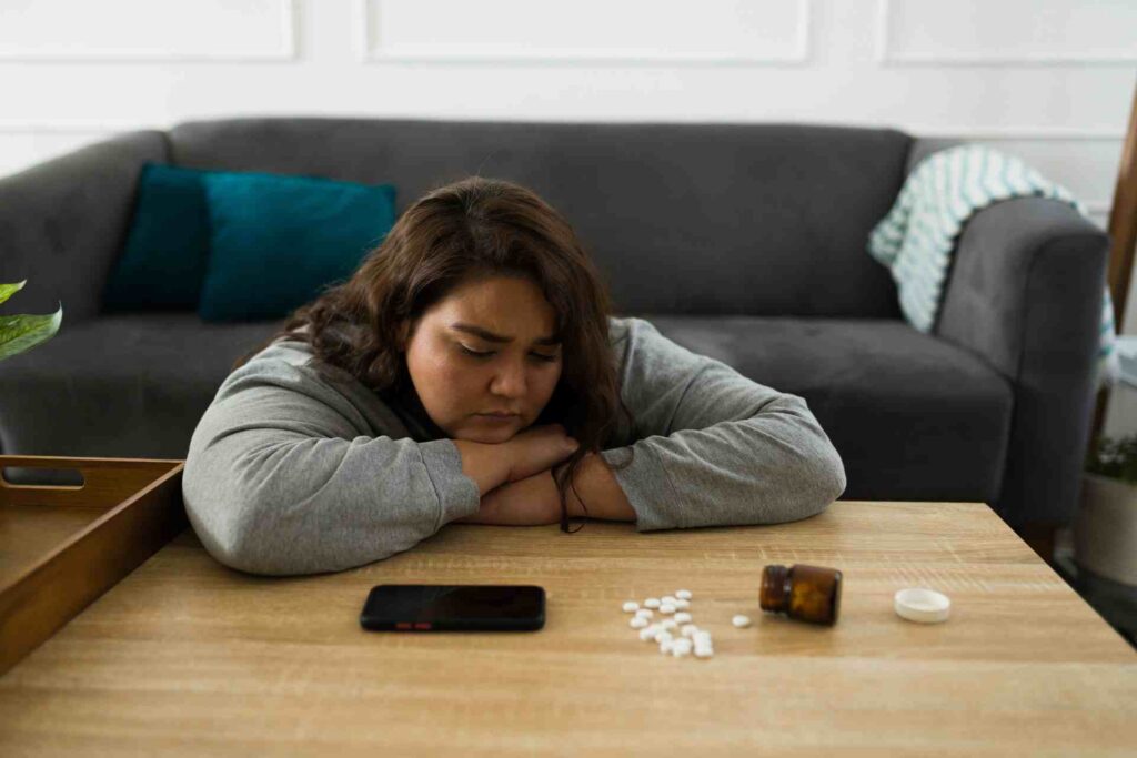 Woman sitting at a table with pills and a prescription bottle, representing prescription drug misuse and substance abuse in Missouri