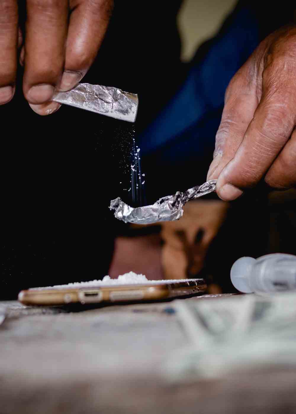 Hands preparing heroin with foil and powder for injection drug use