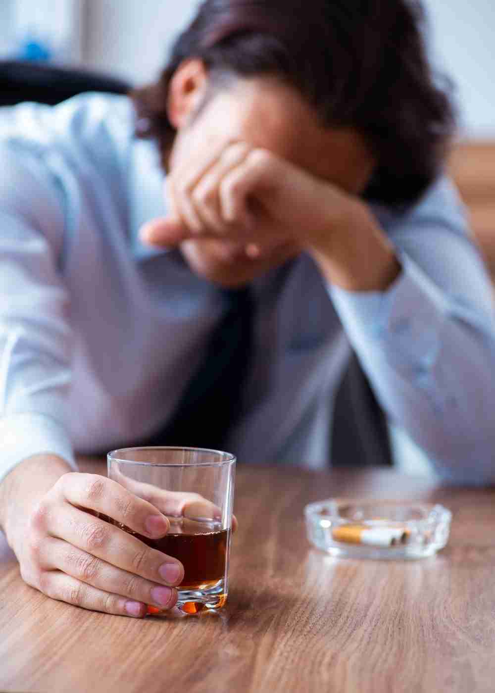 Person holding a glass of alcohol while appearing emotionally distressed and overwhelmed