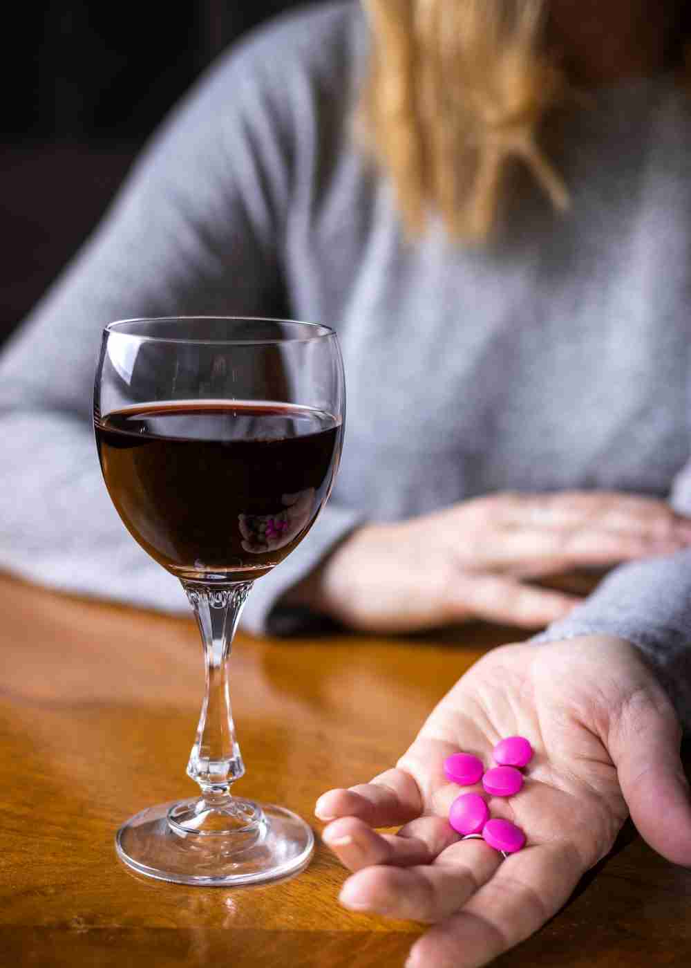 Glass of wine beside a person's hand holding pills, illustrating the dangers of mixing alcohol and prescription medications