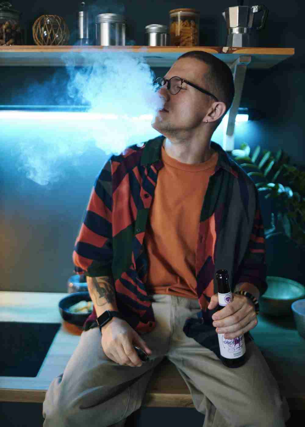 Young adult vaping while holding an alcoholic beverage, illustrating substance use and addiction risk